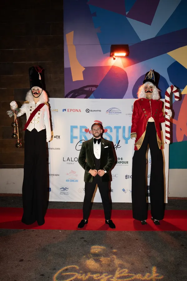 A host in a velvet tuxedo between two nutcracker stilt walkers